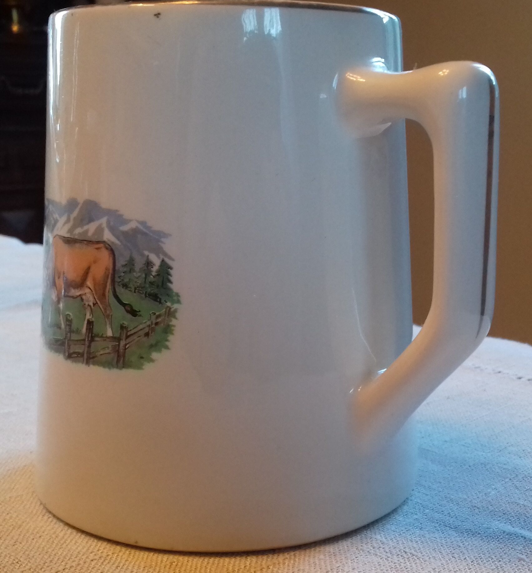 Pot à Lait en faïence des années 30, motif : une vache dans un champ avec montagnes en fond.