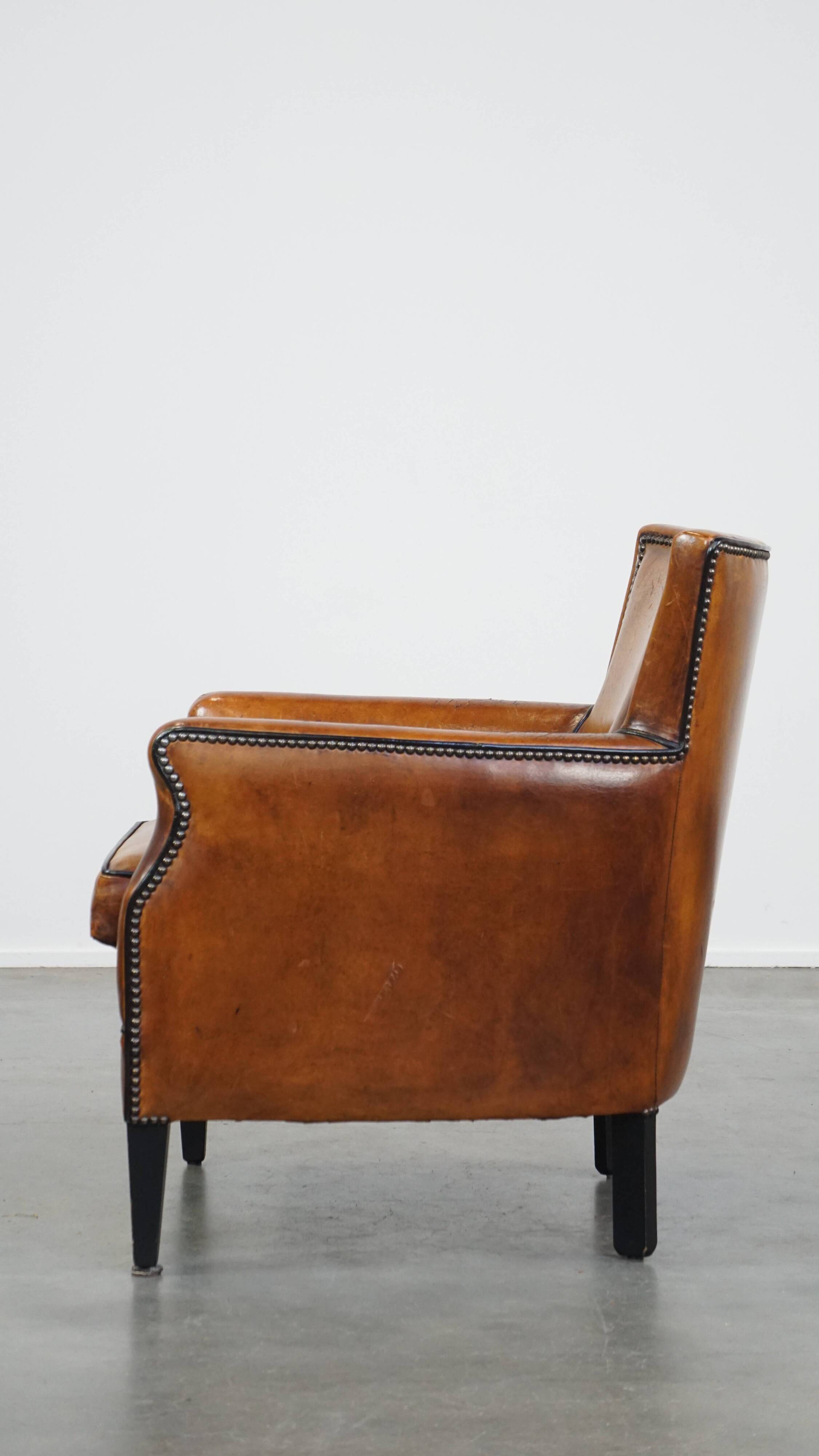Cognac-colored sheepskin armchair with black piping and decorative nails