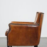 Cognac-colored sheepskin armchair with black piping and decorative nails