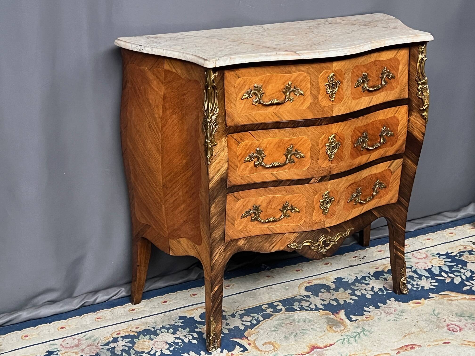 Louis XV style commode with rosewood veneer, gilded bronze mounts, and marble top.