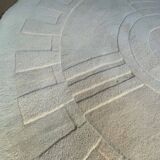 Round ecru rug with geometric relief patterns in wool