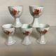 Five old egg cups with orange and grey flowers, polygonal base.