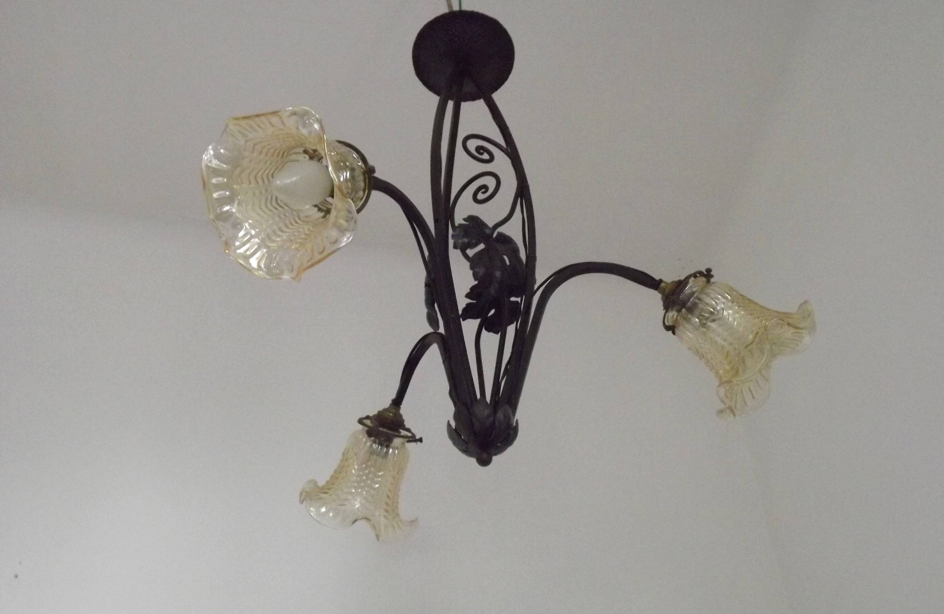 French Art Nouveau leaf detail iron three-light chandelier with amber glass shades.