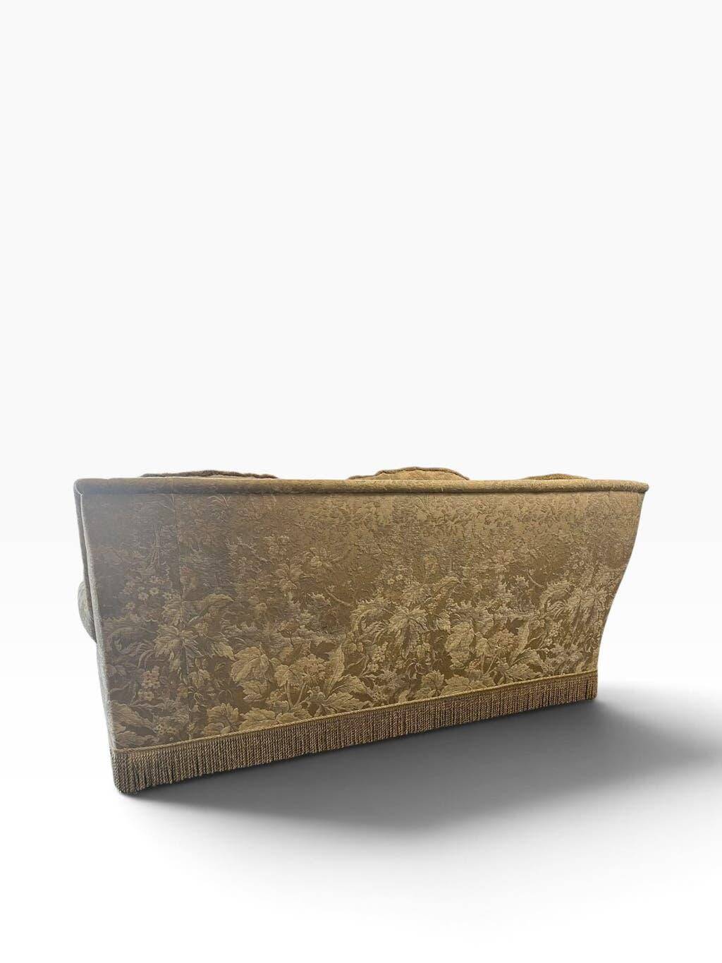 Vintage beige three-seater sofa with floral pattern and fringes.