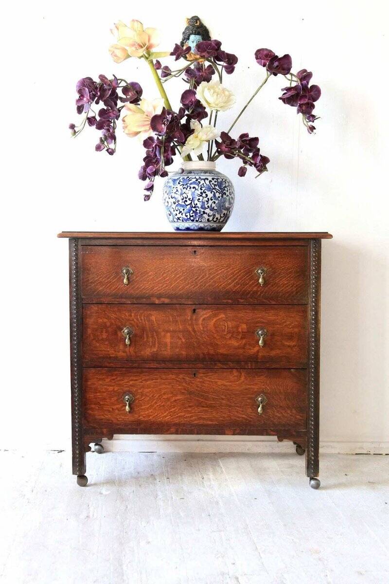 Antique oak chest of drawers on castors with brass handles and carved details