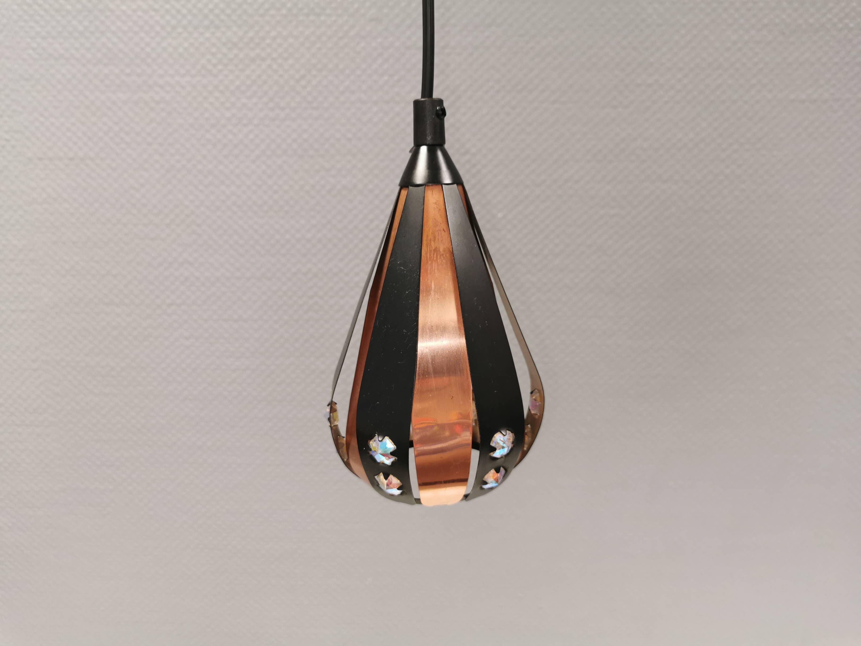 A teardrop-shaped pendant lamp made of copper, black metal, and prisms.