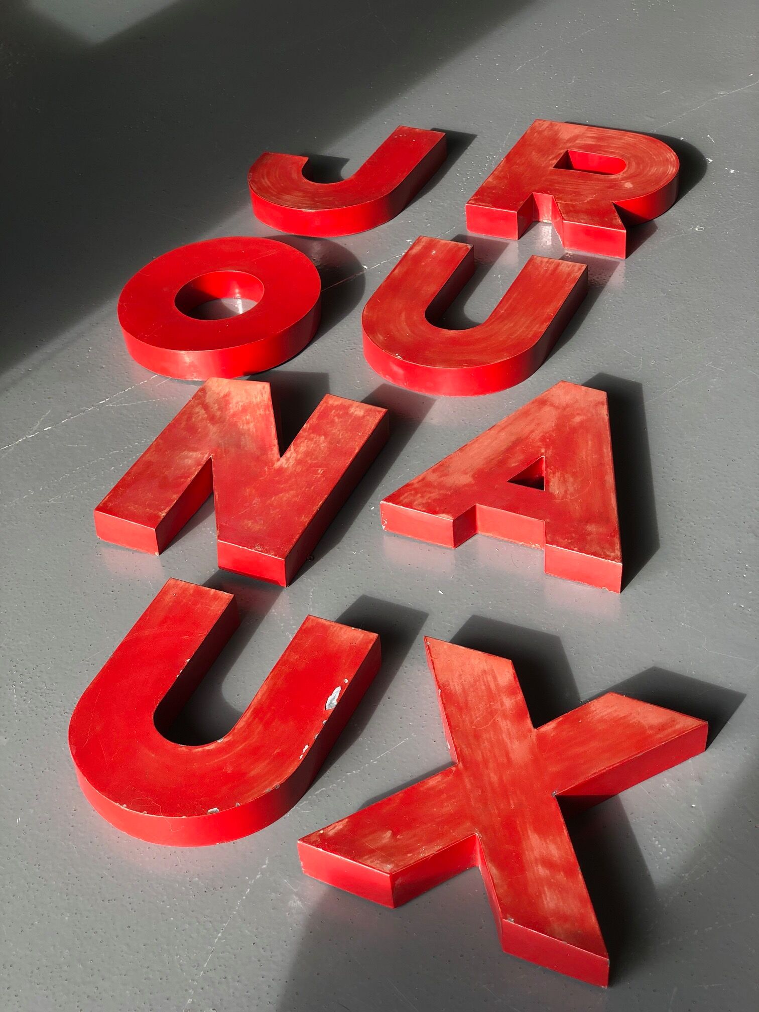 Lettres d'enseigne en zinc rouge formant le mot JOURNAUX