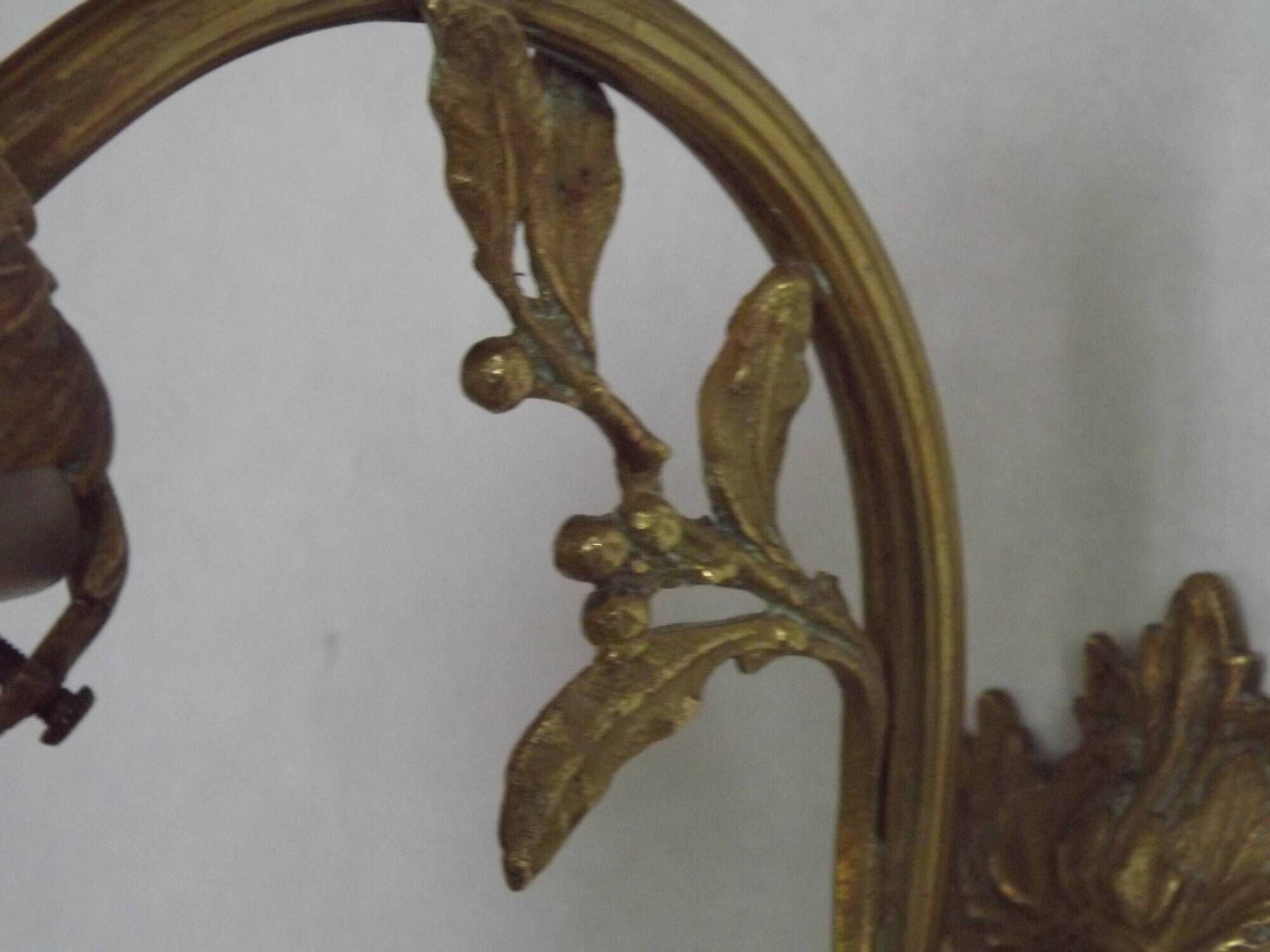 Simple wall sconce in French Art Nouveau bronze with a white glass shade featuring patterns.