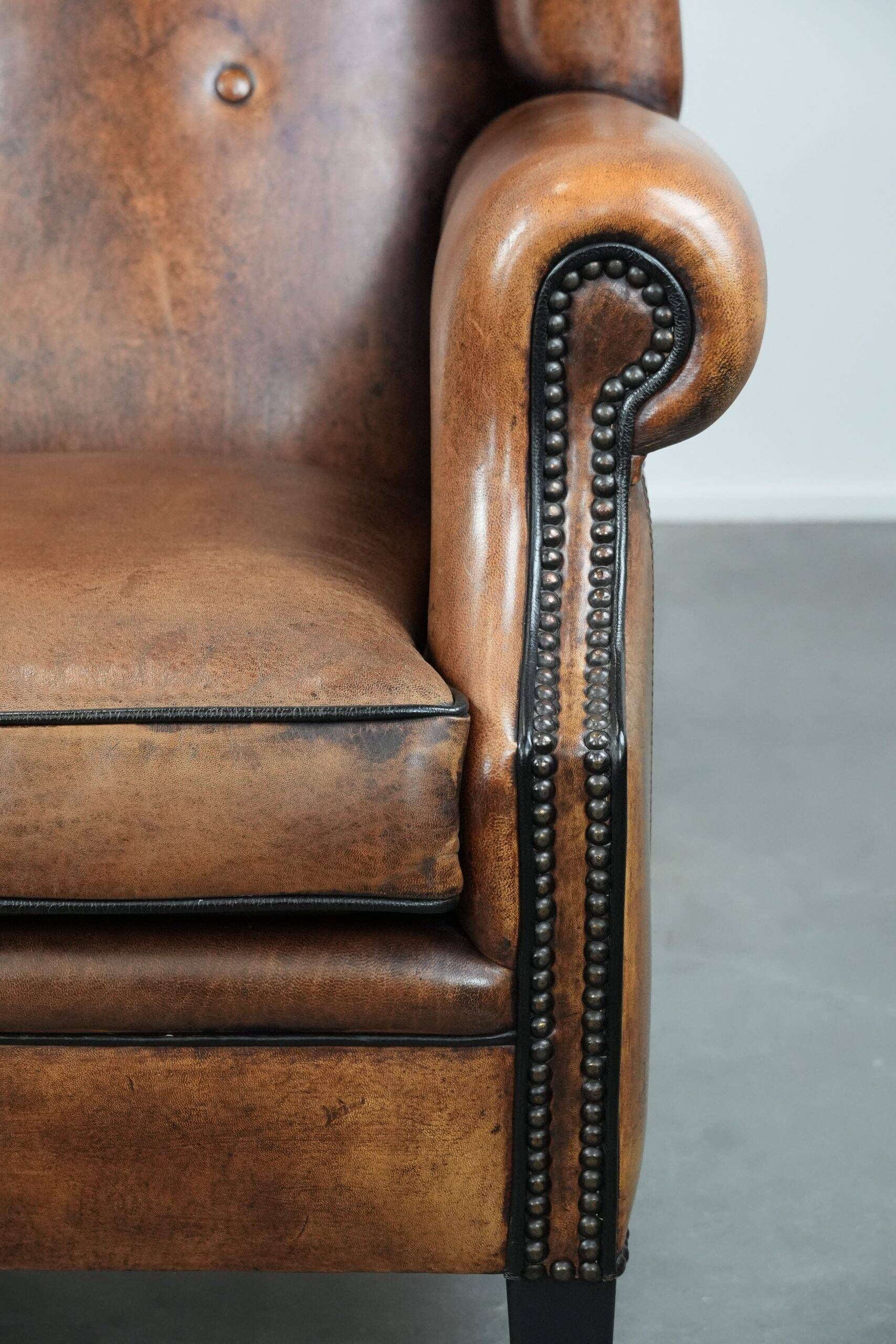 Sheepskin wingback armchair with decorative nails and black piping