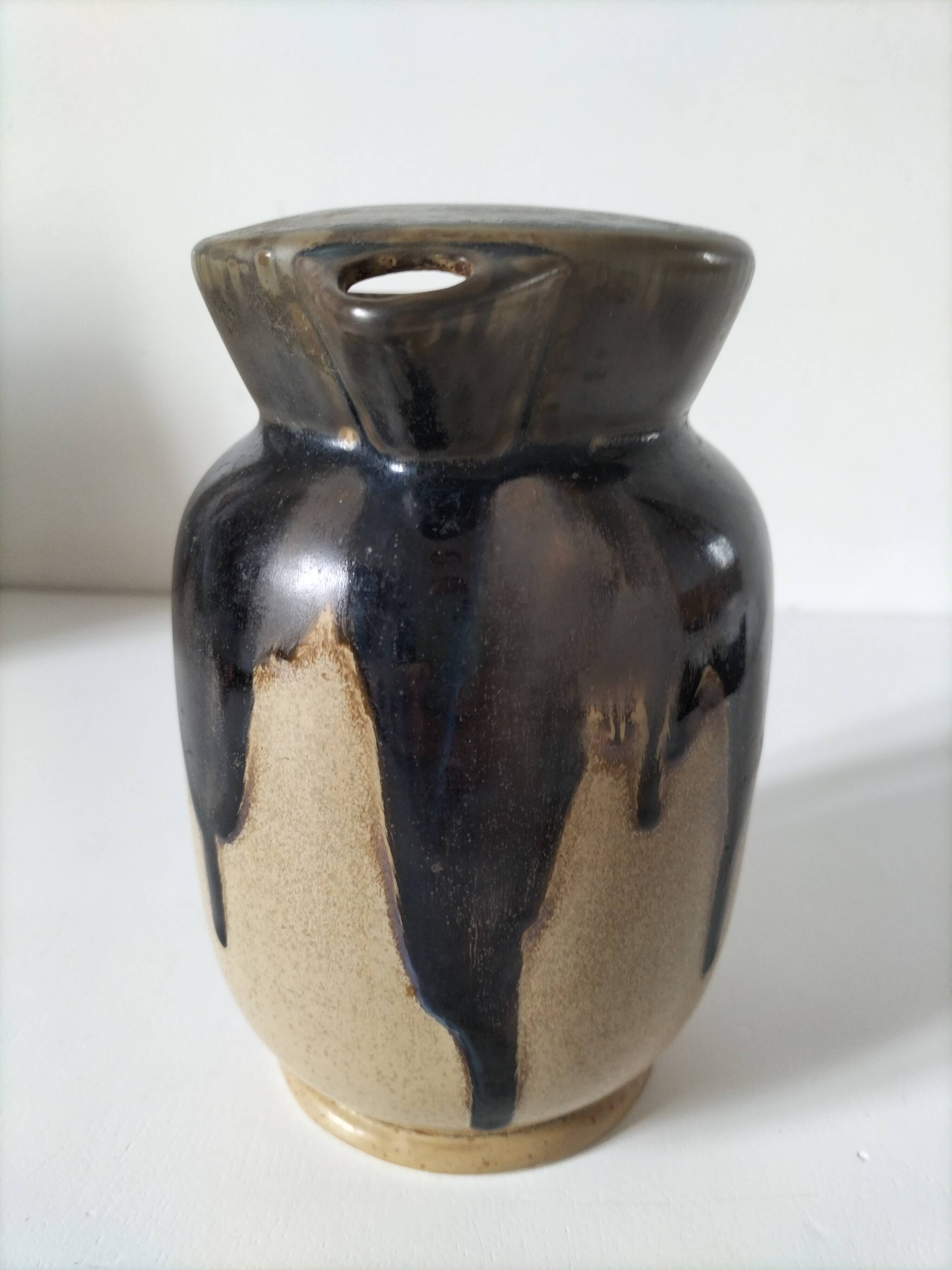 Stoneware jug with deep black drips on a sandy background.