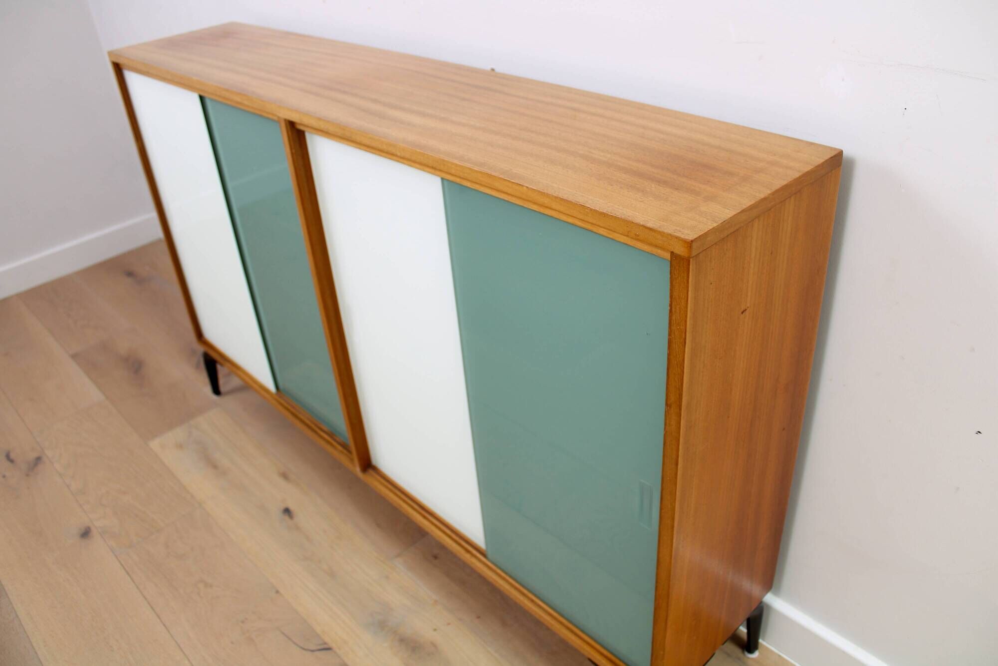 A vintage mid-century bookshelf/sideboard with green and white sliding door