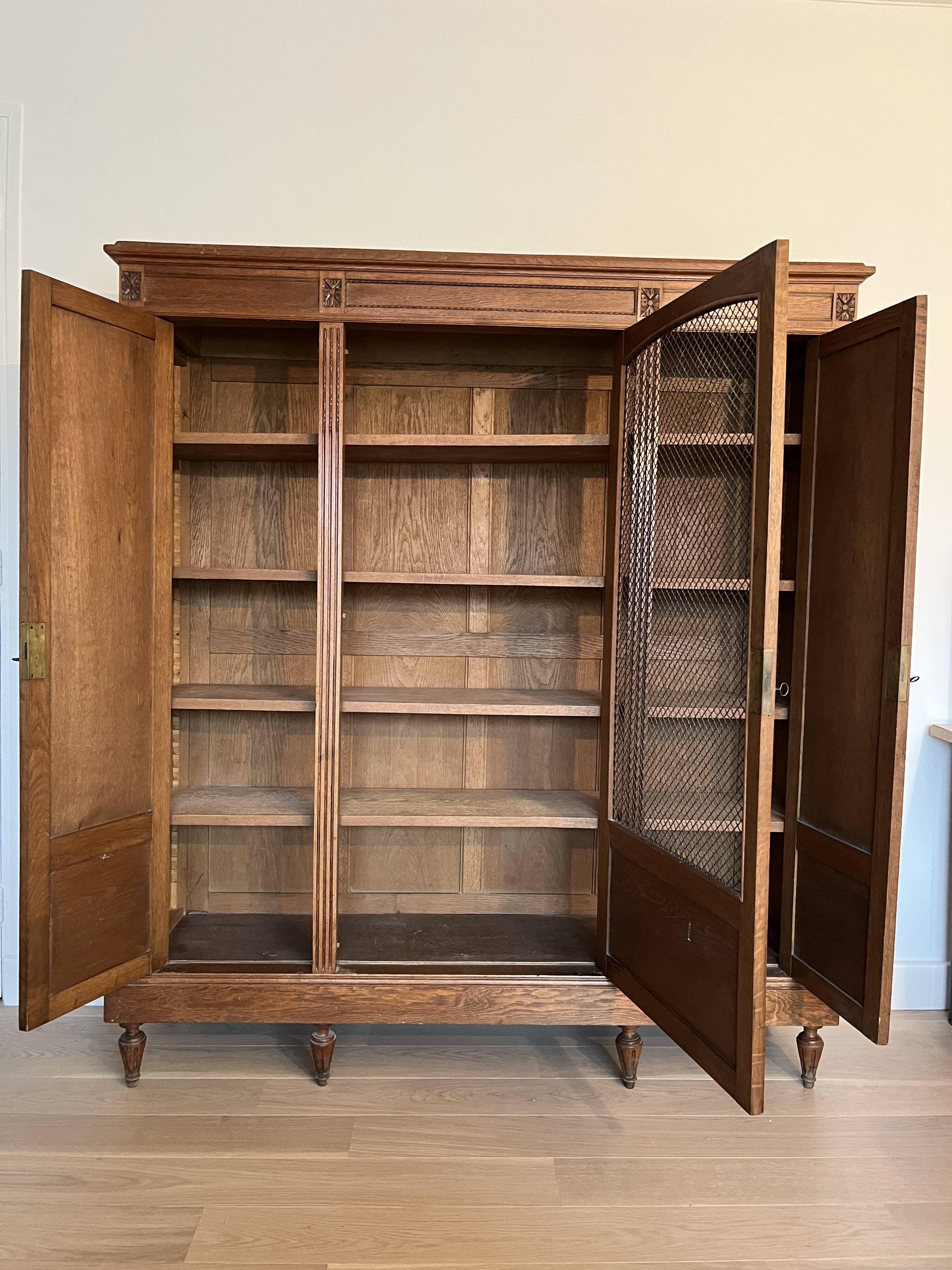 Three-door glass display cabinet with a grille in the Louis XVI style, antique and decorated.