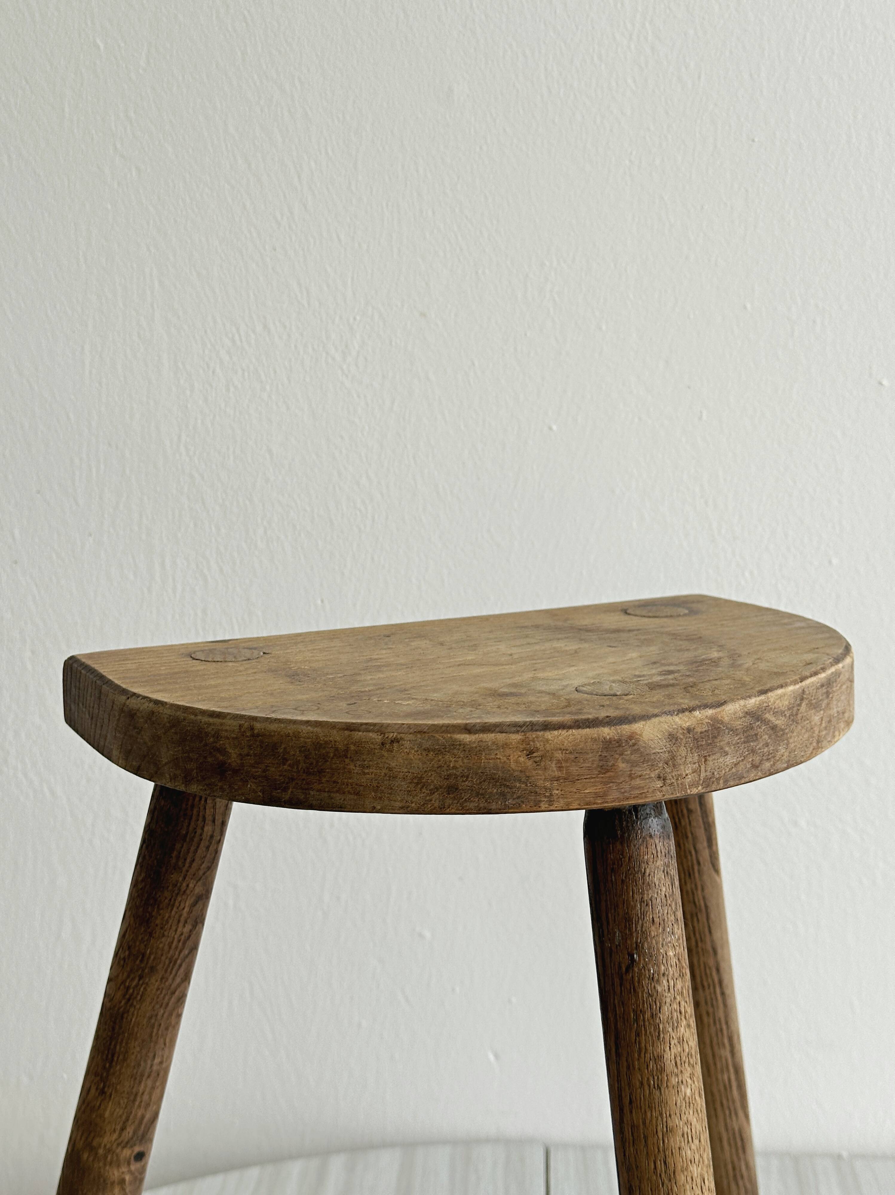 Small antique tripod stool in light wood, half-moon seat.