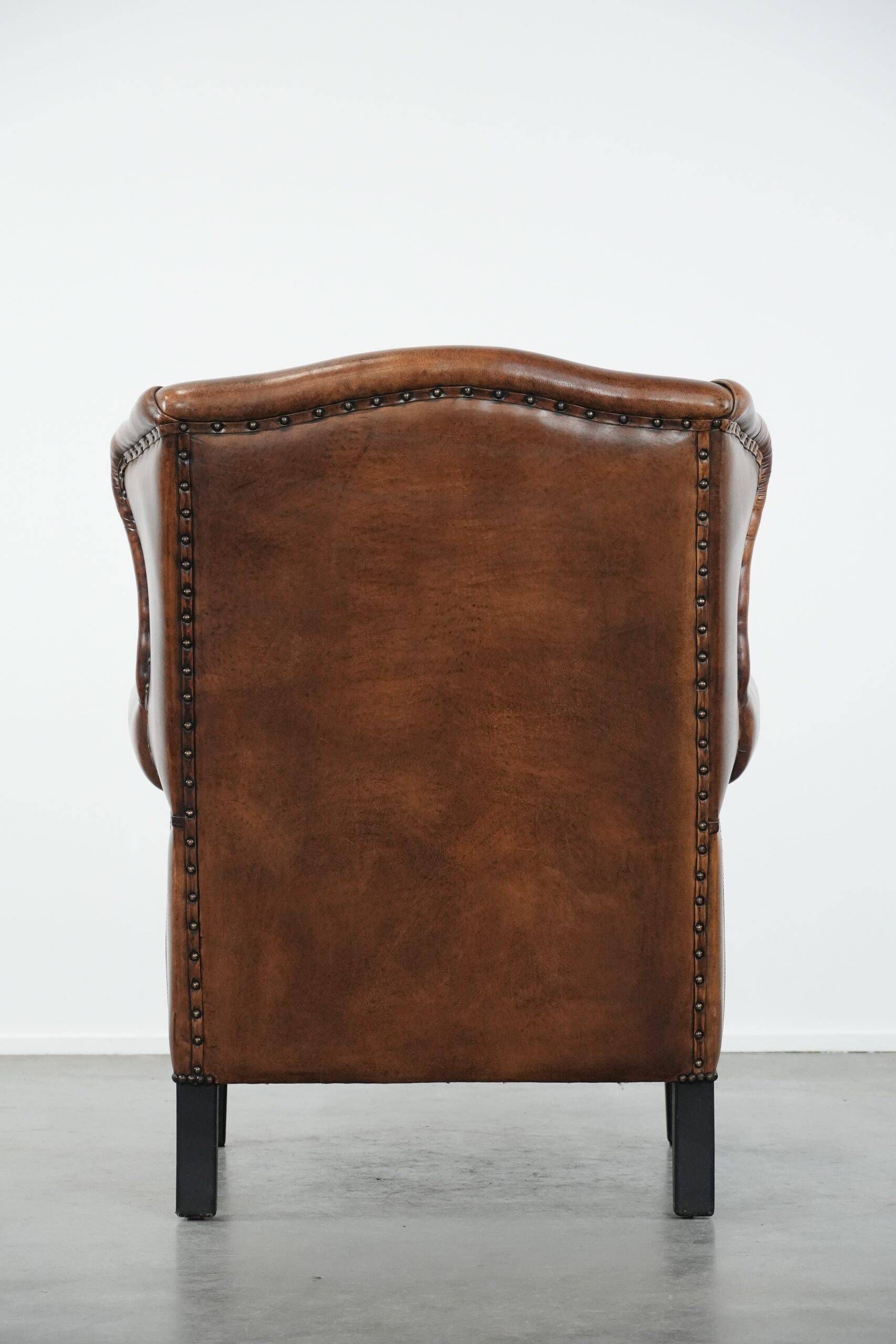 Sheepskin wingback armchair with decorative nails and black piping
