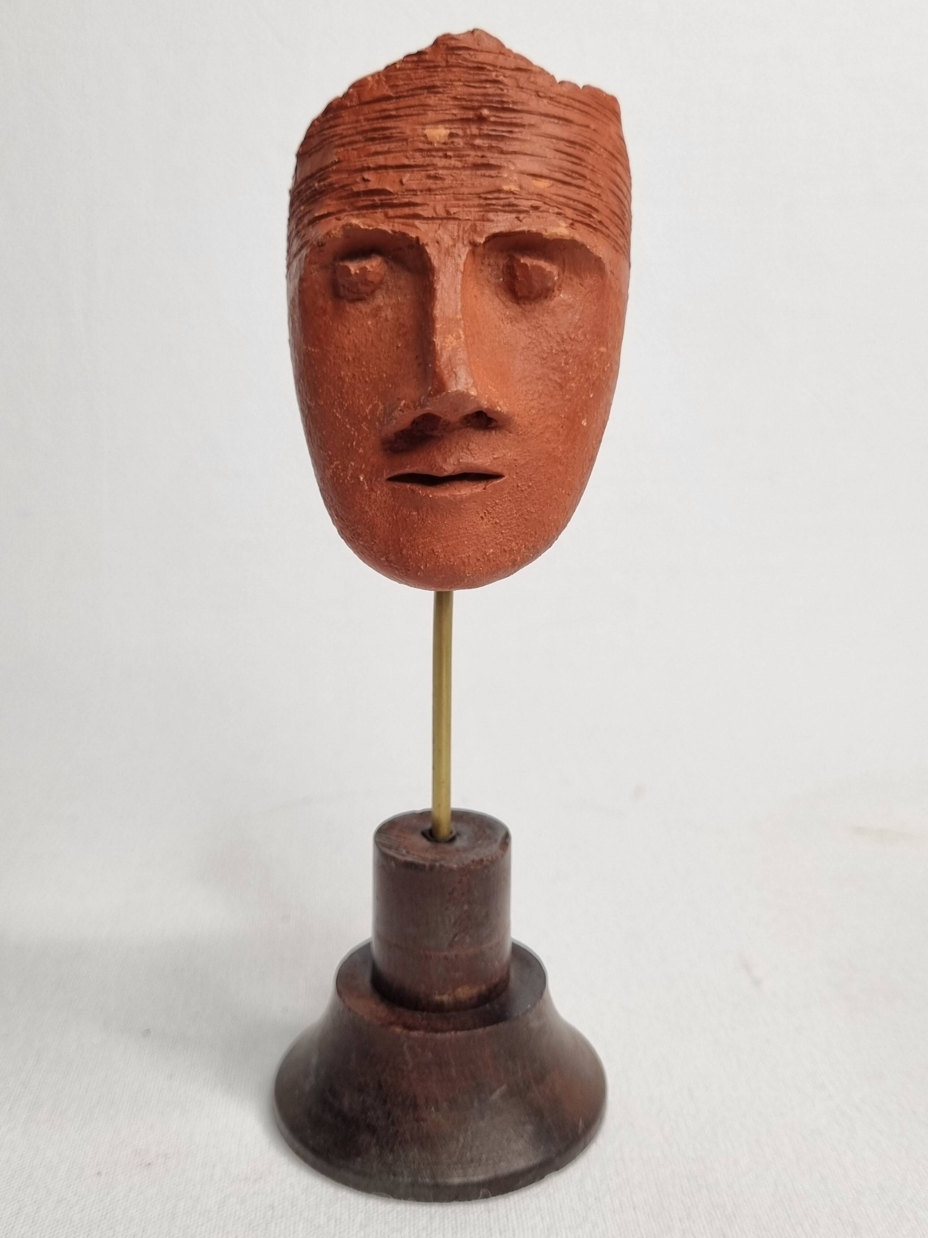 Stylized head in patinated ochre terracotta on a dark wooden base, 17 cm