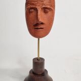 Stylized head in patinated ochre terracotta on a dark wooden base, 17 cm