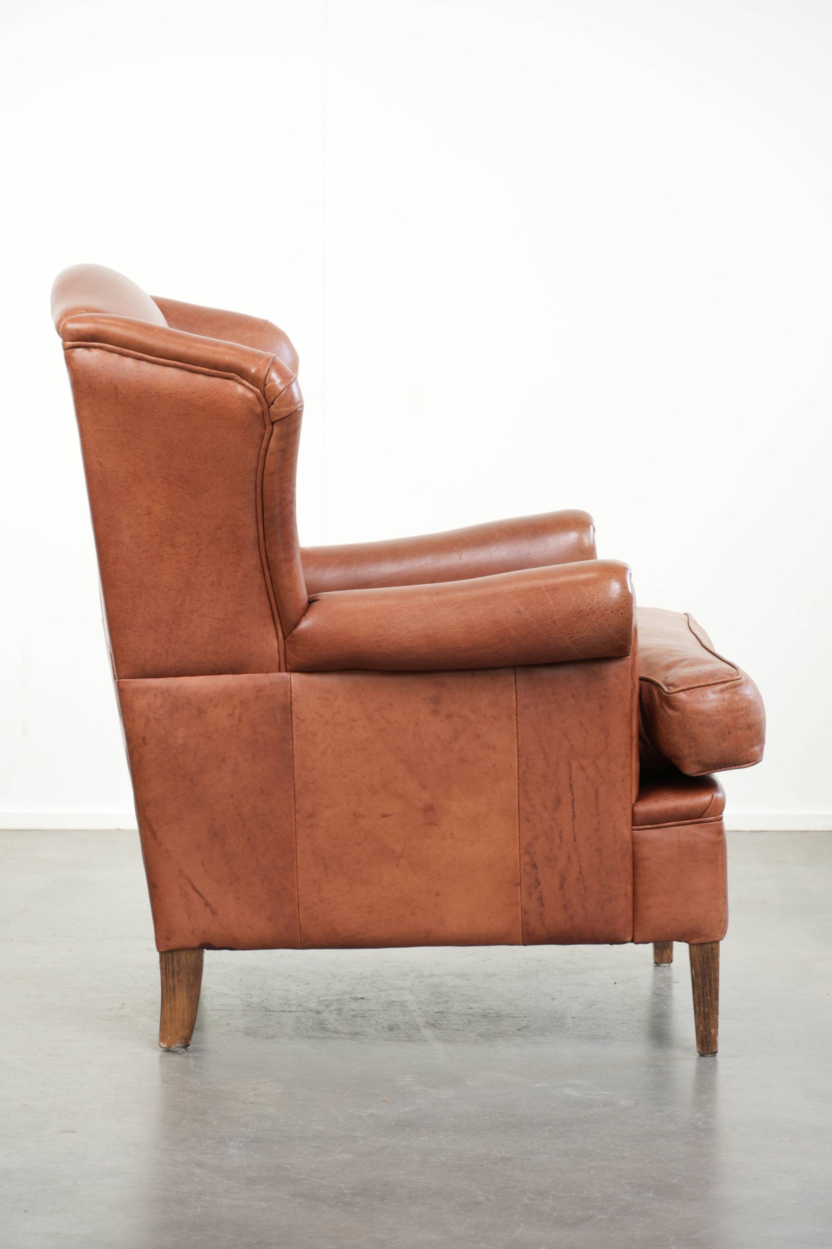 Fauteuil anglais à oreilles de couleur cognac clair en cuir de vache.