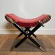 Neoclassical curule stool in red leather, decorated with crossed swords in bronze and metal covered in black leather.