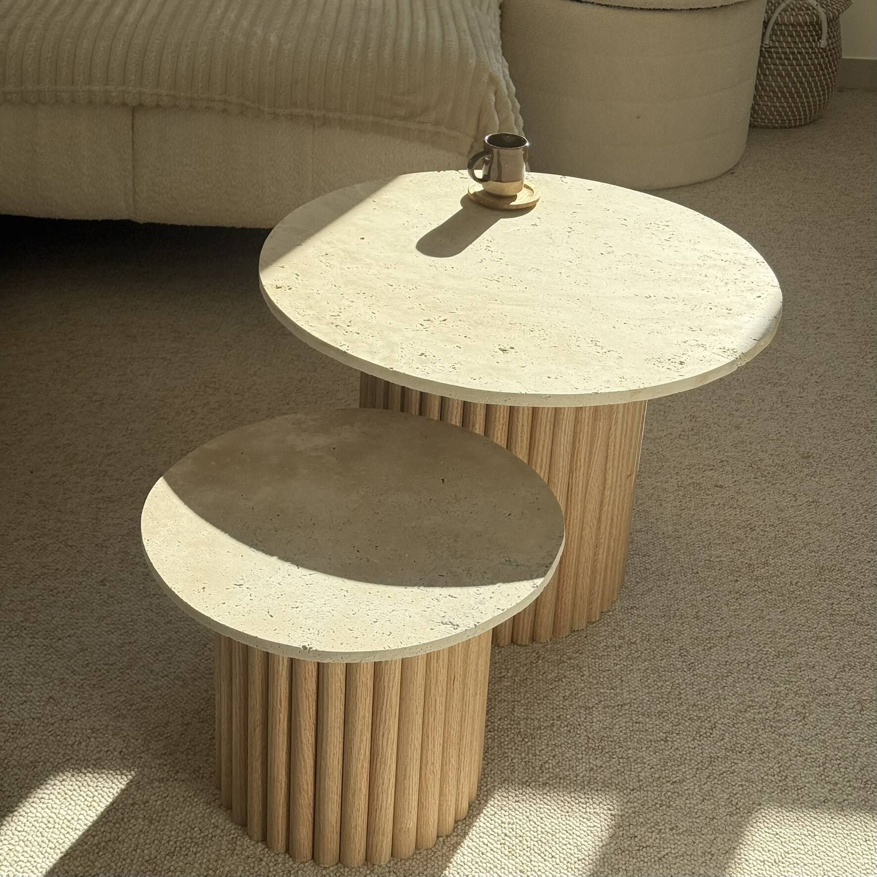Round nesting coffee table in travertine and raw fluted wood.