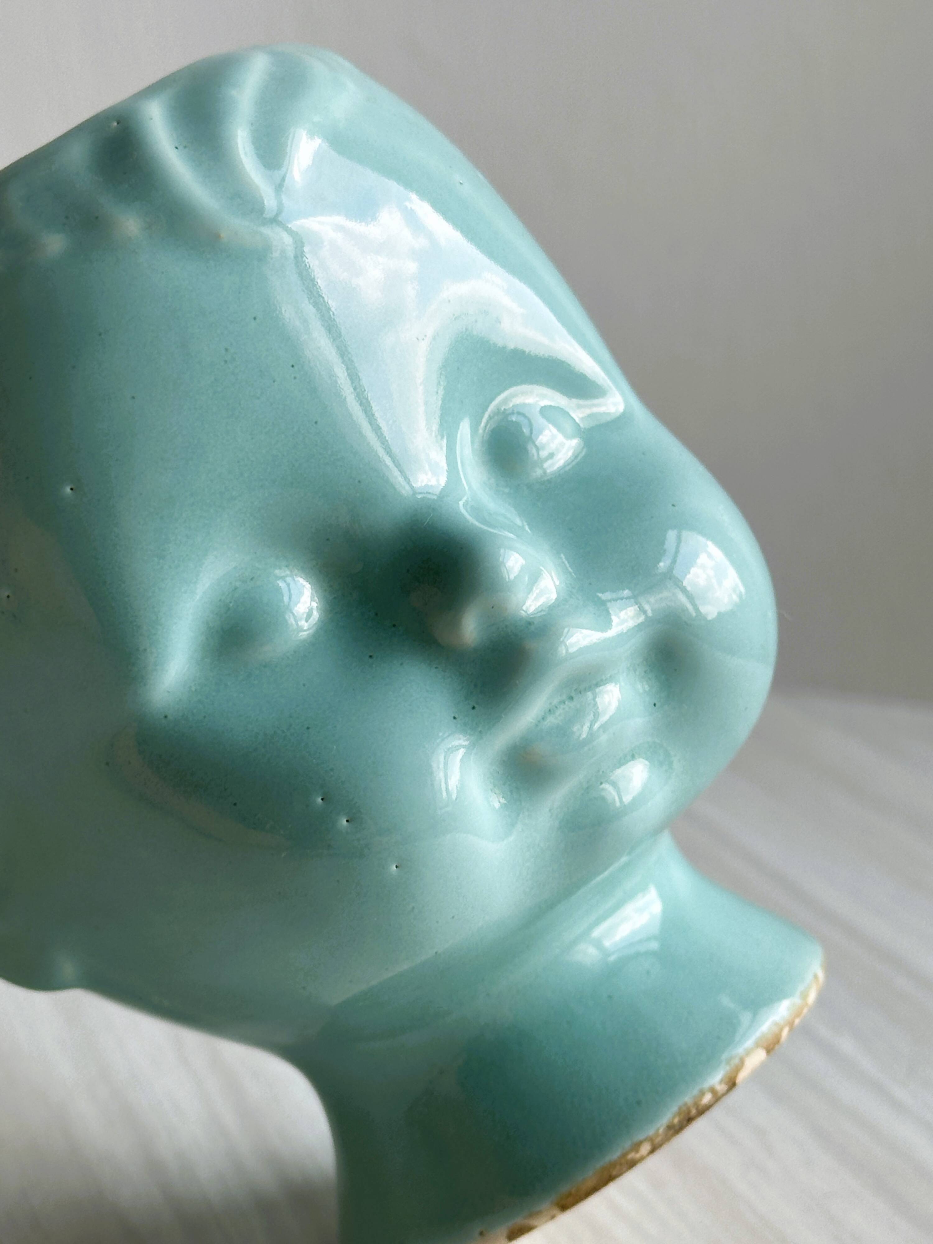 Turquoise plant pot in the shape of a vintage doll's head.