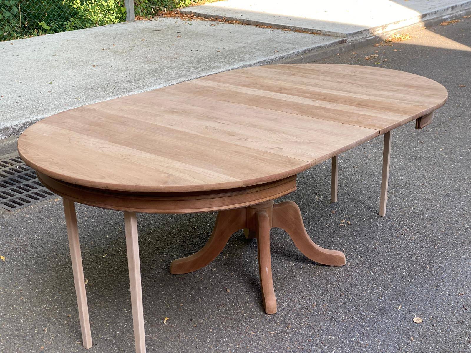 Large extendable round dining table stripped in solid cherry wood with a central leg.