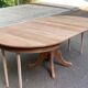 Large extendable round dining table stripped in solid cherry wood with a central leg.