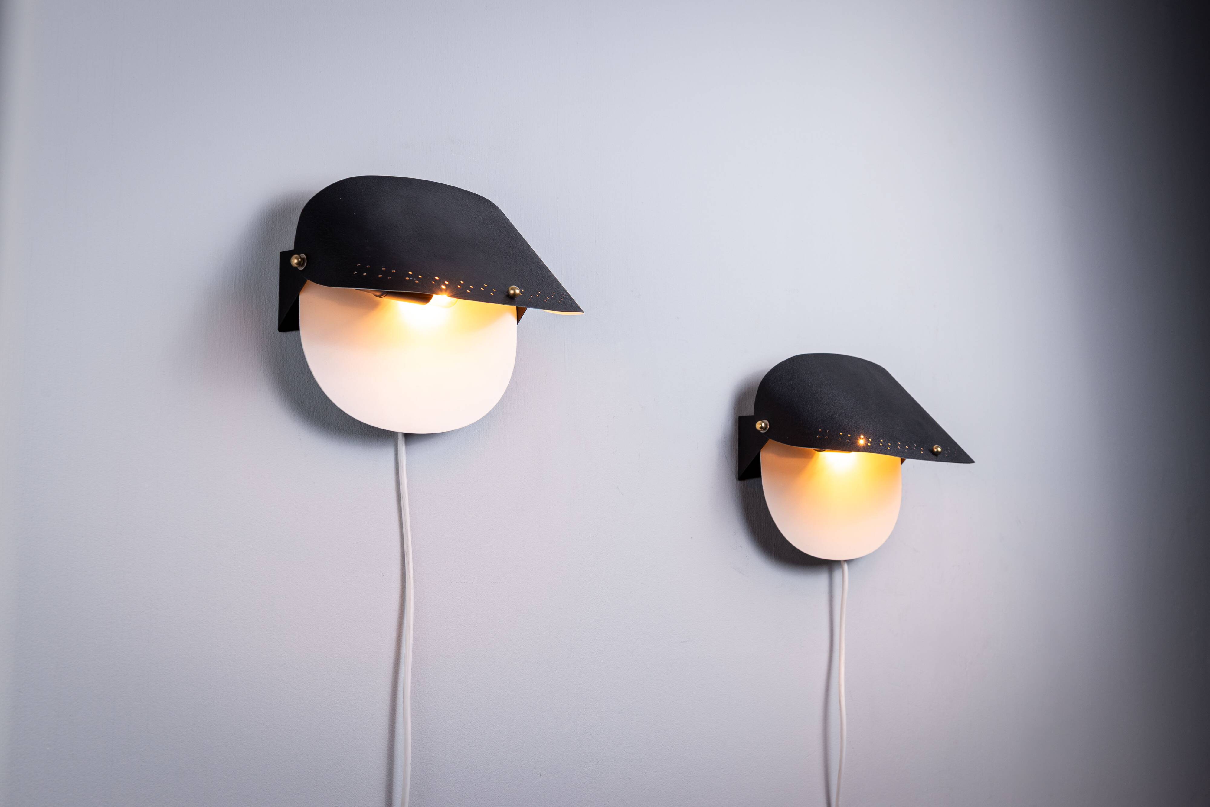 Matte black wall lamps with perforated shades and brass details