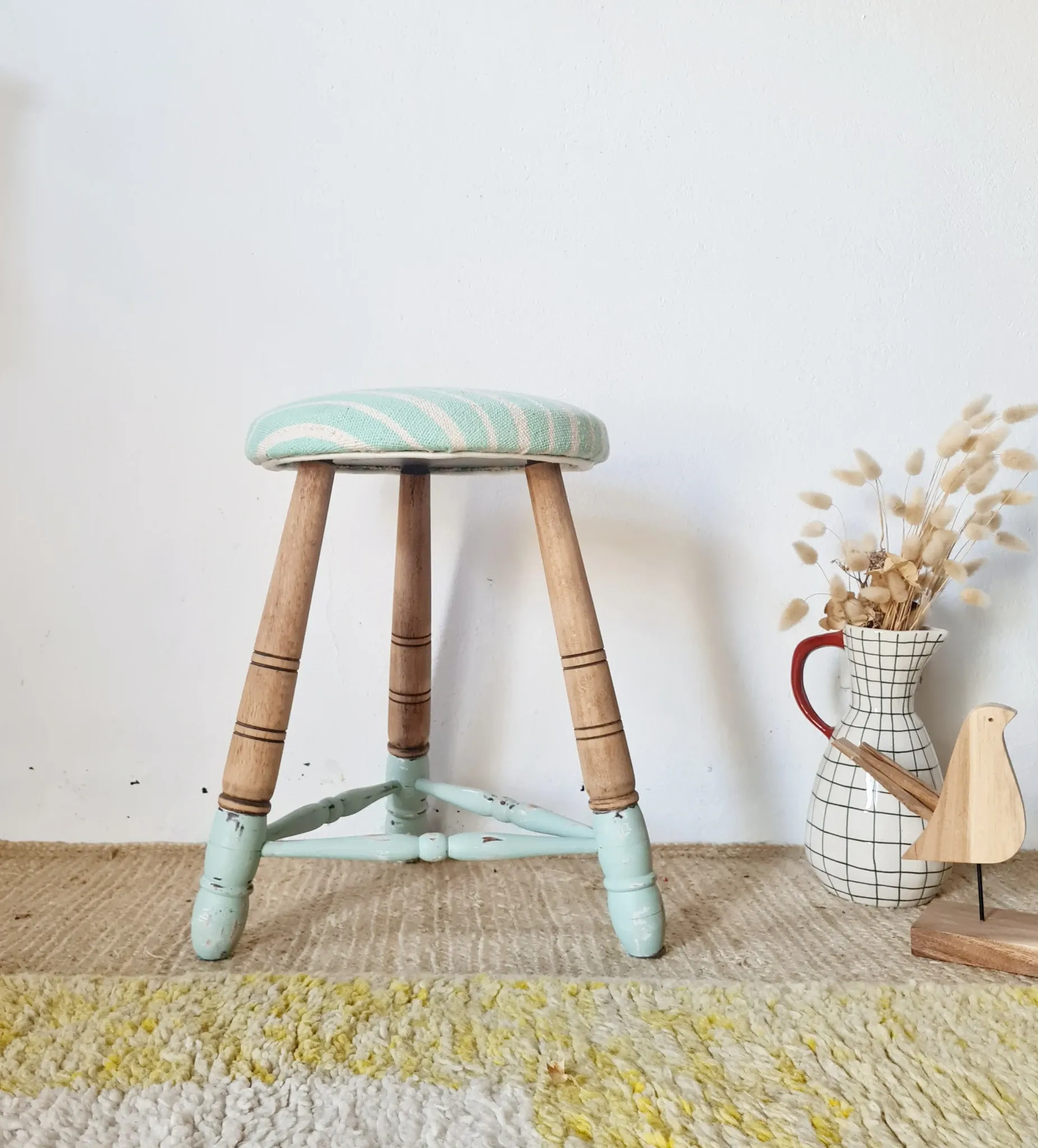 Antique tripod stool with blue striped seat.