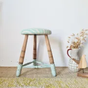 Antique tripod stool with blue striped seat.