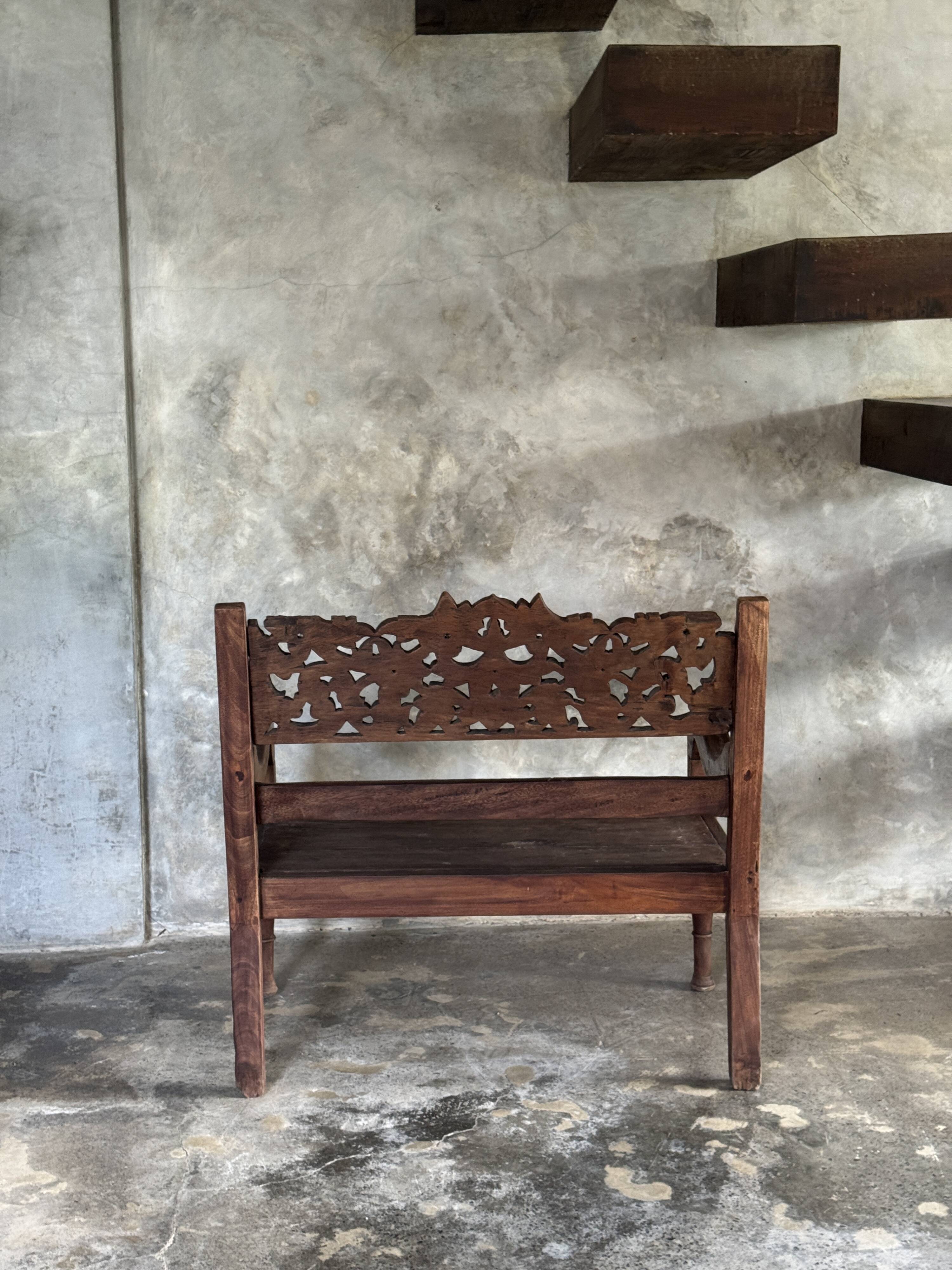 Small antique Indonesian bench in carved teak with plant and floral motifs.