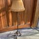 Art Deco floor lamp in bronze metal with a straw yellow fabric shade, twisted shaft, and tripod base.