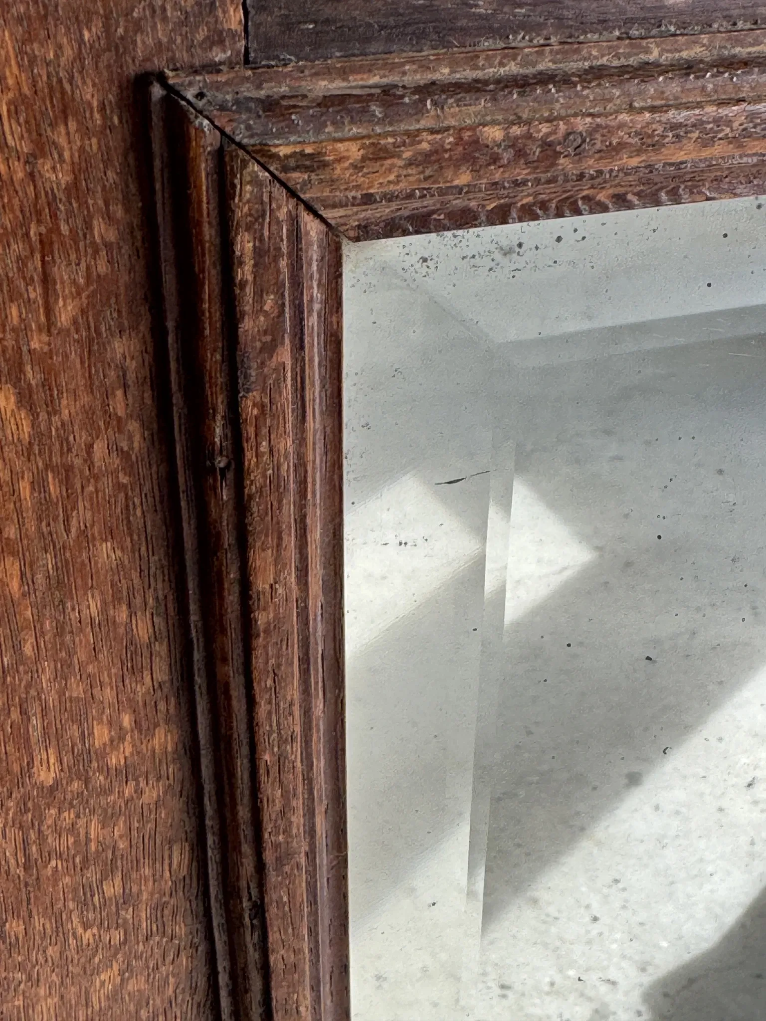 Antique mirror door (left) of a brown oak wardrobe with bevelled glass.