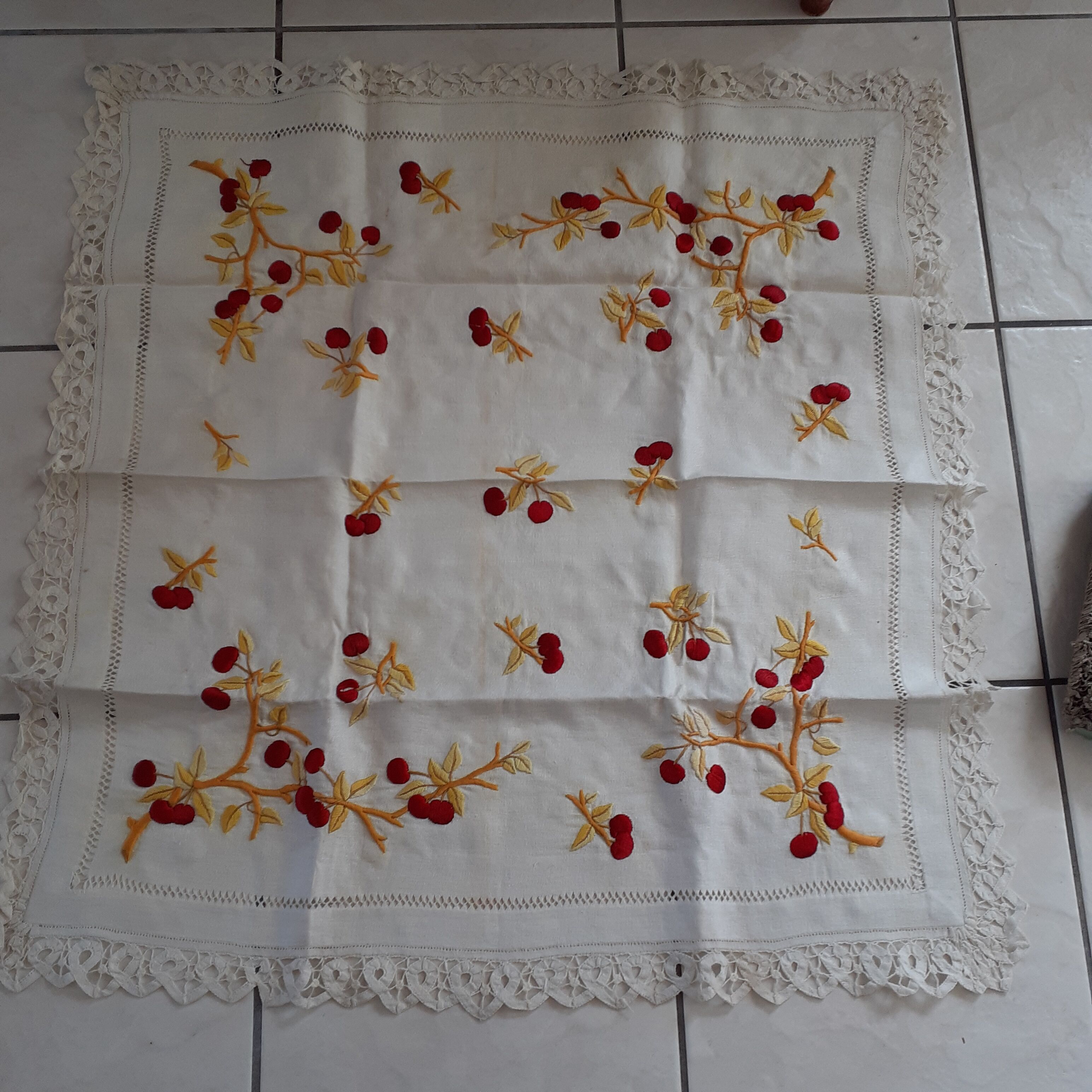 Square white doily. Embroidered with red tantrums. Lace entourage and days.