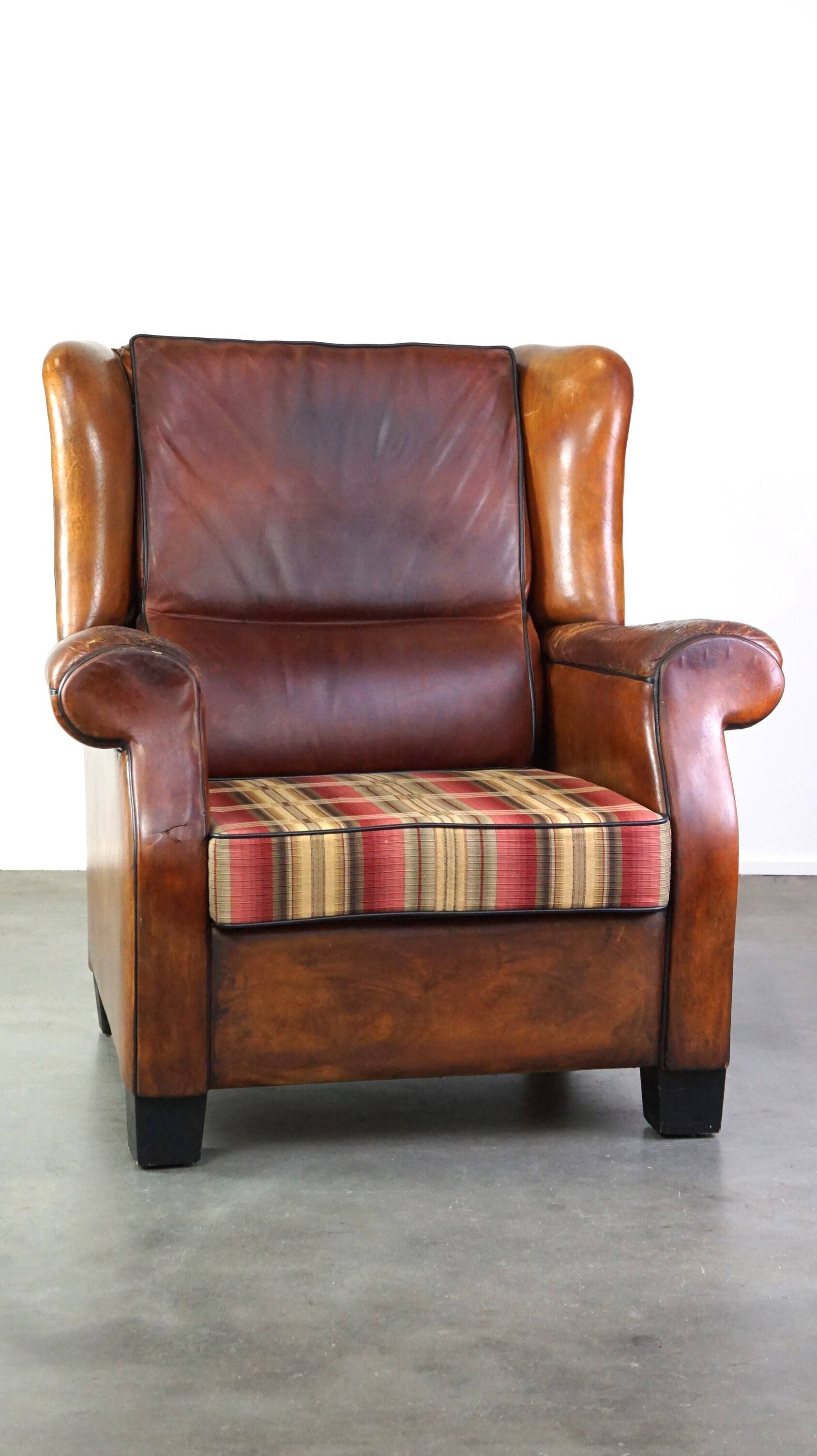 Very large worn sheepskin wing chair with a checked seat cushion