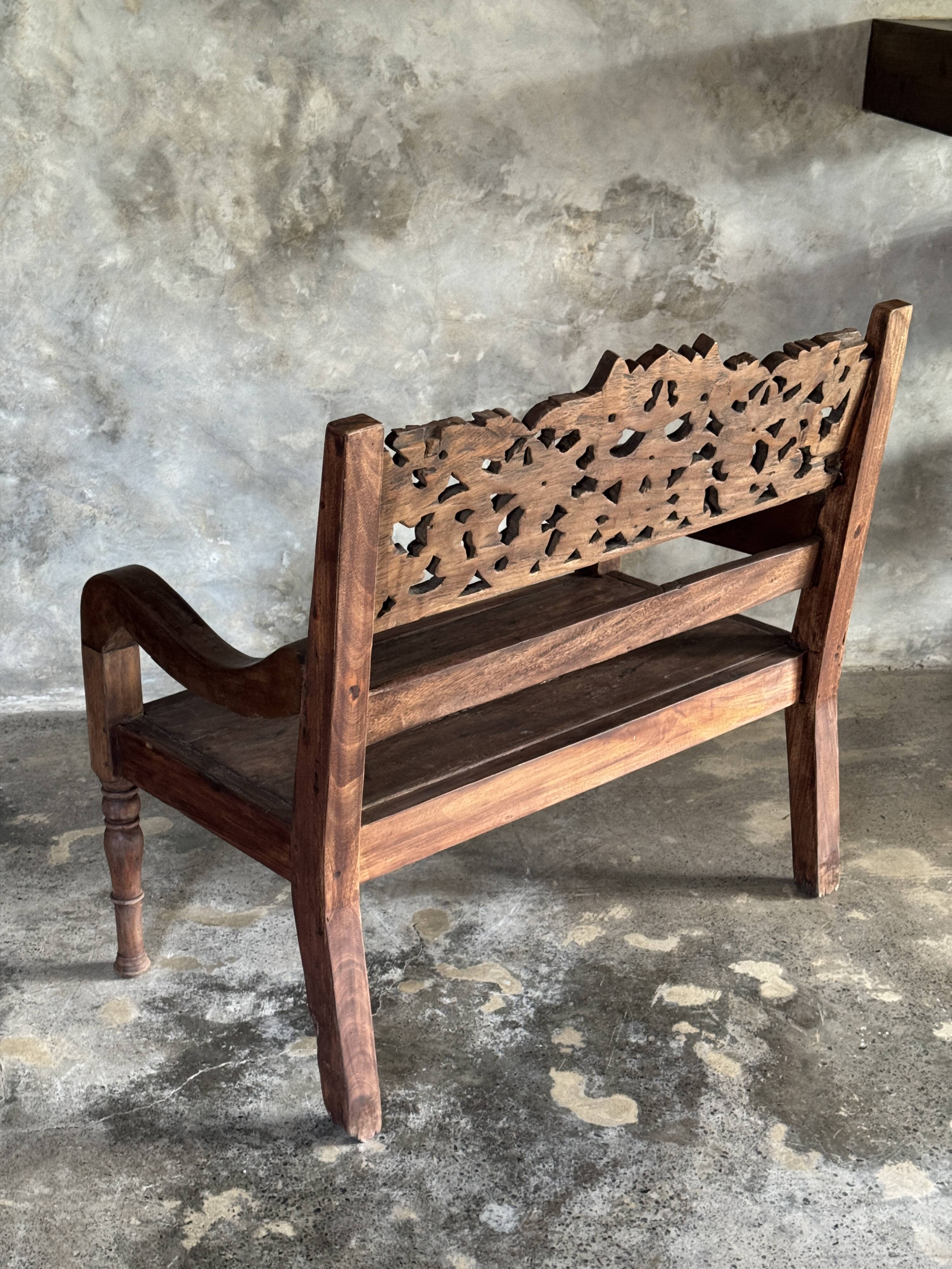 Small antique Indonesian bench in carved teak with plant and floral motifs.