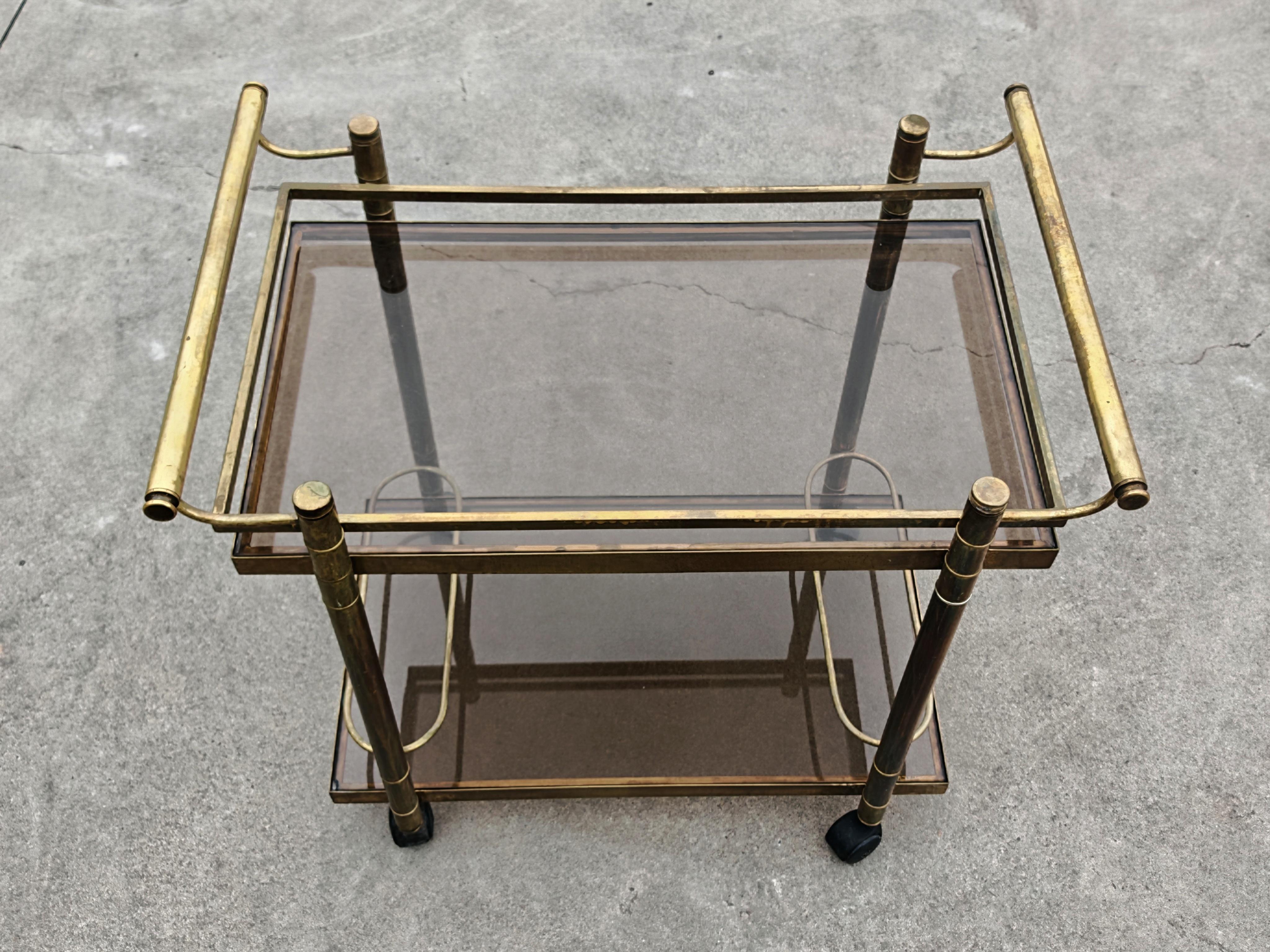 Mid Century Modern bar cart with 2 levels in brass and tinted glass.
