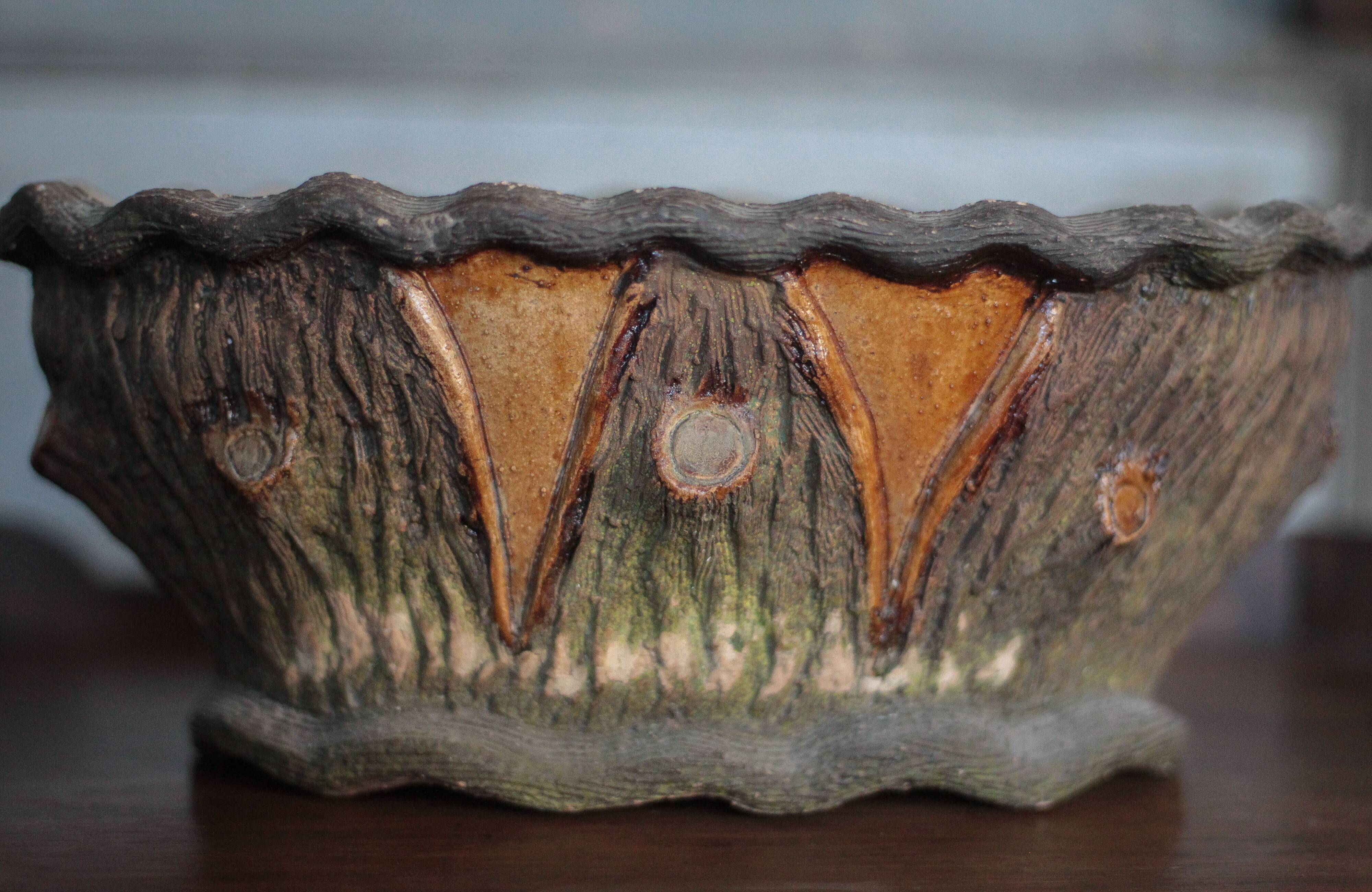 Terracotta planter in a brutalist style resembling a tree trunk, pot cover, countryside.