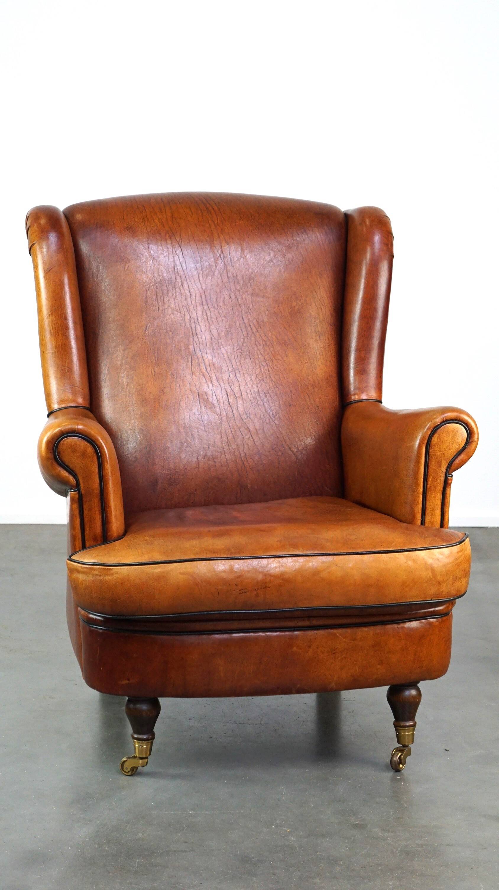 Subtle sheepskin wing chair in good condition on brass front wheels