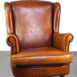 Subtle sheepskin wing chair in good condition on brass front wheels