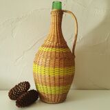 Vintage glass bottle covered with hand-woven wicker and scoubidou, with a handle