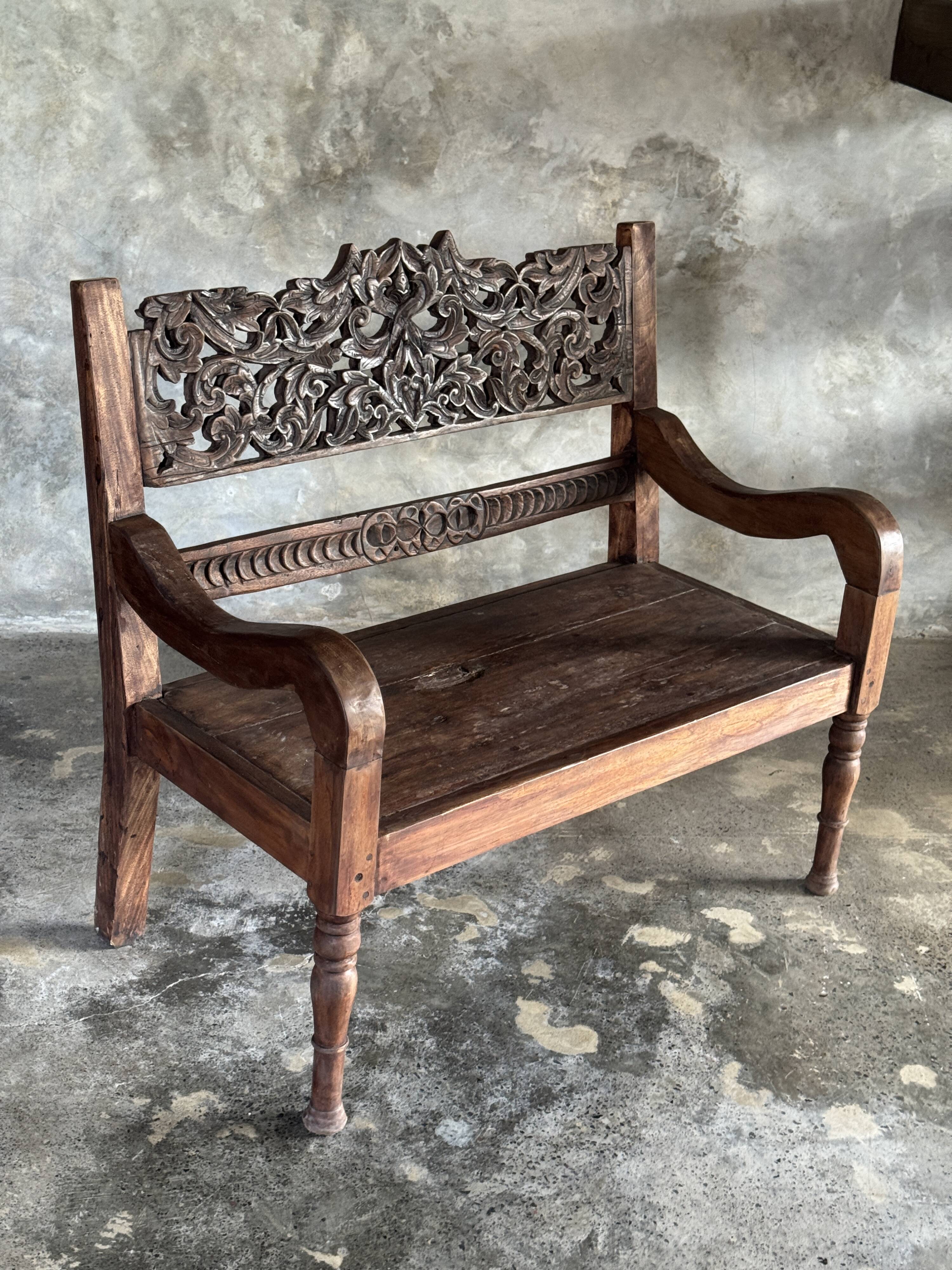 Small antique Indonesian bench in carved teak with plant and floral motifs.