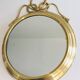 Large decorative oval mirror in brass adorned with a significant twisted bow.