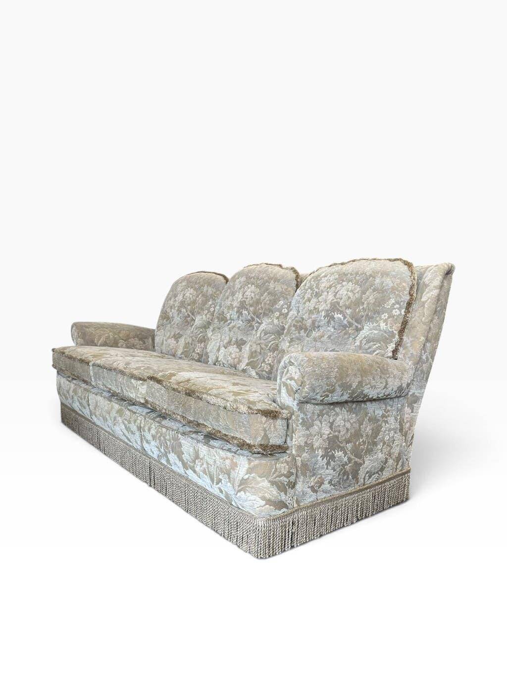 Vintage beige three-seater sofa with floral pattern and fringes.