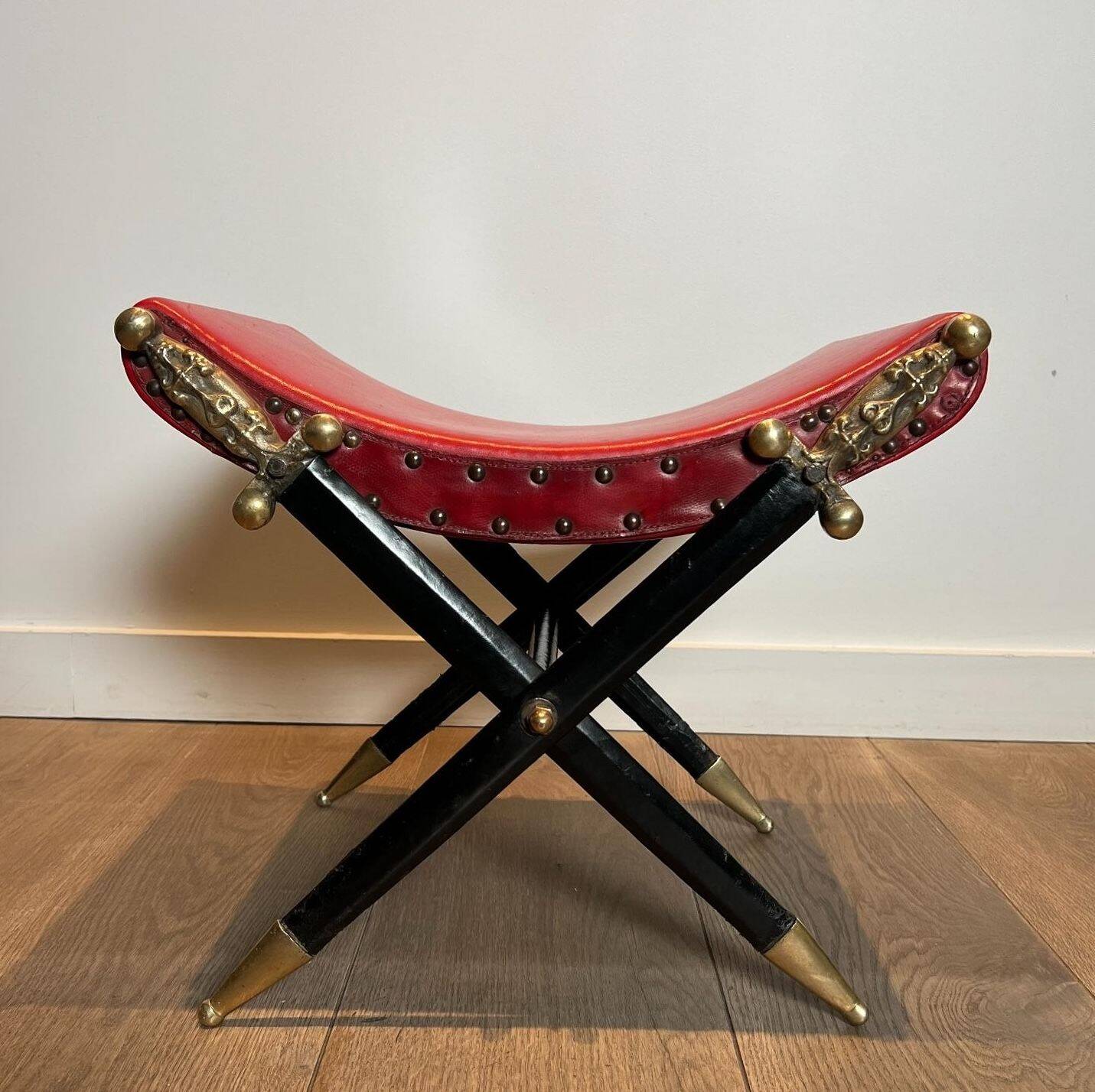 Neoclassical curule stool in red leather, decorated with crossed swords in bronze and metal covered in black leather.