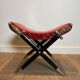 Neoclassical curule stool in red leather, decorated with crossed swords in bronze and metal covered in black leather.