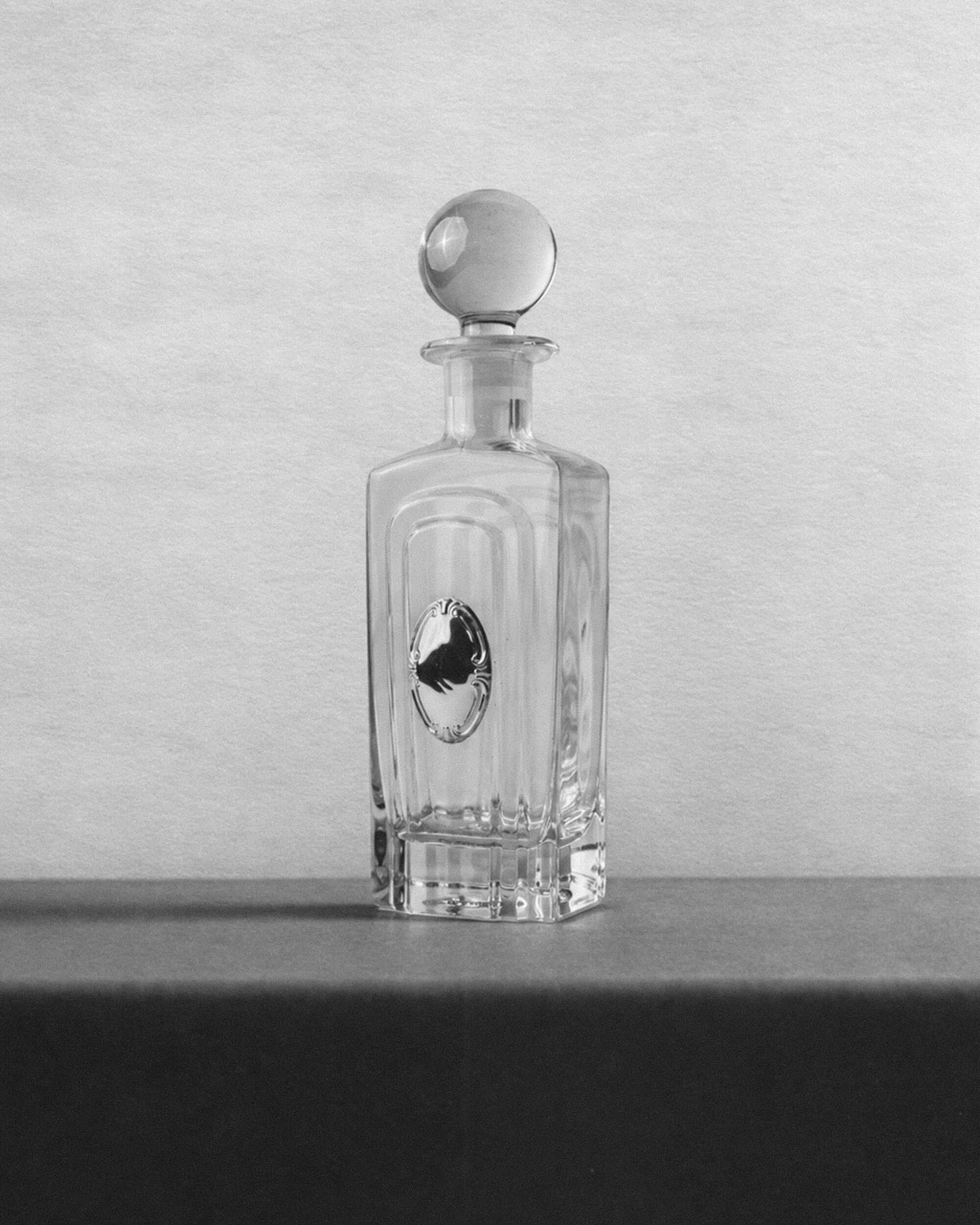 Vintage glass decanter from the 1980s, transparent glass with a silver plate and spherical stopper.