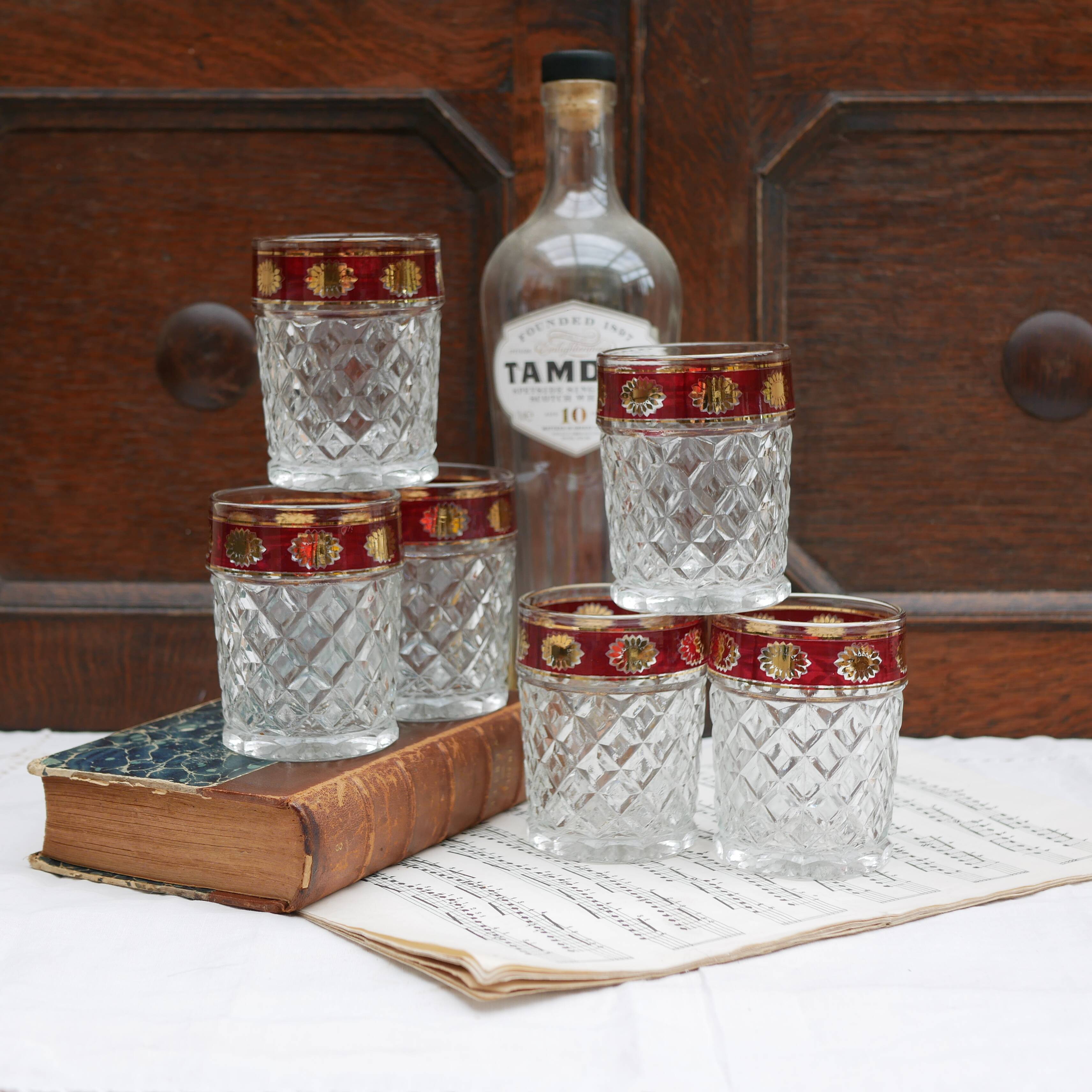 Six pressed glass whisky glasses with red and gold rims