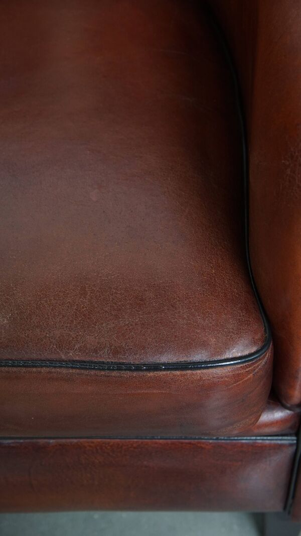 Fauteuil club en peau de mouton dans une couleur chaude et profonde, fini avec un passepoil noir.