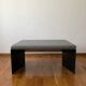 Minimalist/industrial coffee table with a black metal frame and a grey fabric top.