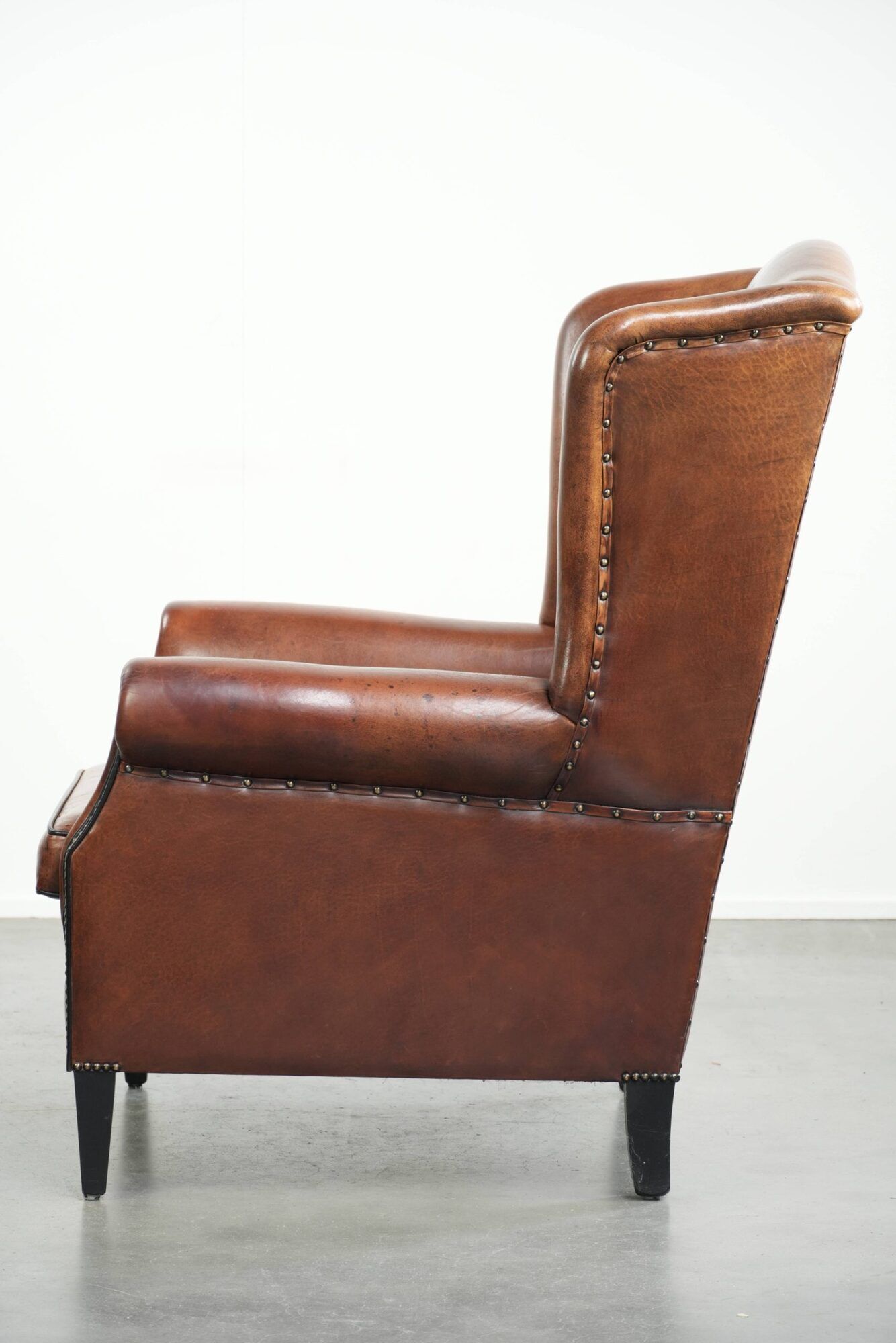 Sheepskin wingback armchair in a warm cognac colour with refined nailhead trim
